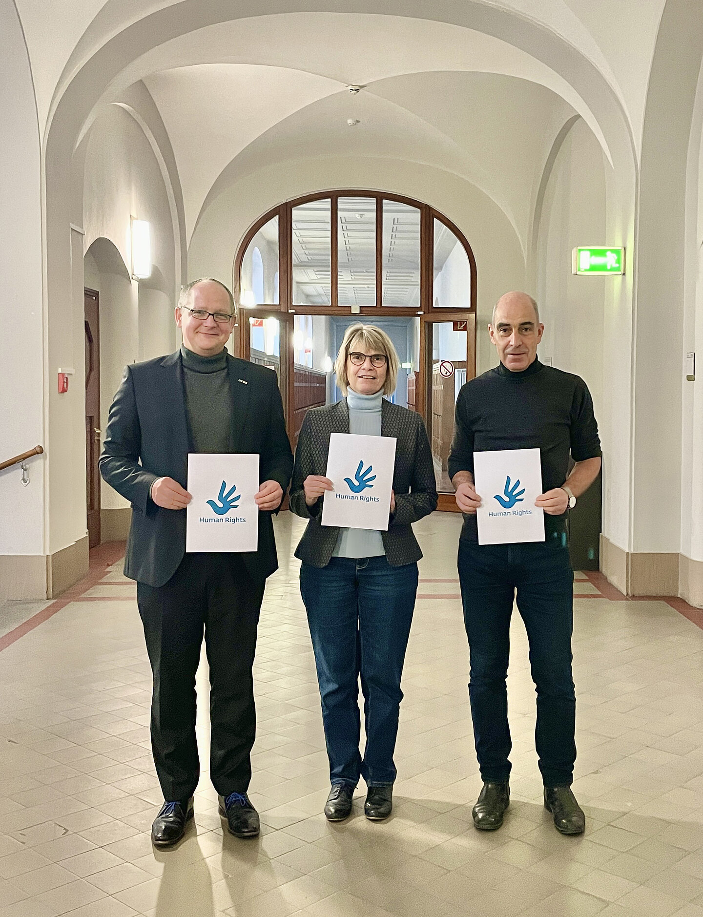 Bekräftigen stellvertretend für die Hochschule Bekenntnis zur Weltoffenheit: Rektor Prof. Mark Mietzner, Prorektorin Bildung Prof.in Barbara Mikus und Prorektor Forschung, Prof. Ralf Thiele. (v.ln.r./Foto: HTWK Leipzig) drei Personen mit Schildern in der Hand stehen auf einem langen Flur