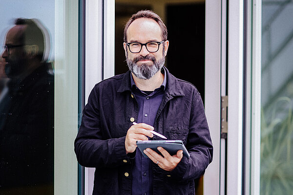 bärtiger Mann mit Laptop lächelt in Kamera