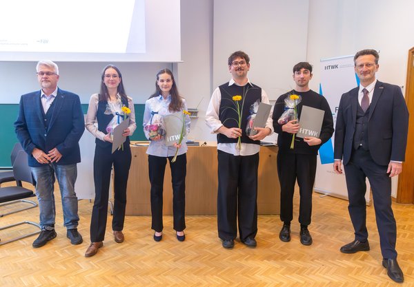 Gruppe von Studierenden mit Urkunden und zwei Professoren steht in einem Hörsaal