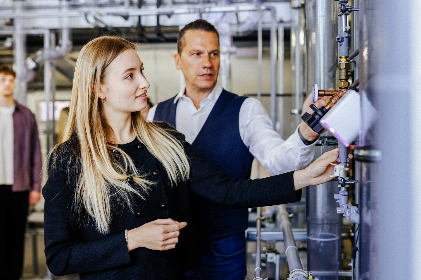 im Vordergrund junge Frau, dahinter Professur - im Wasserturm an Röhren, Prof. Guzek erläutert Funktion