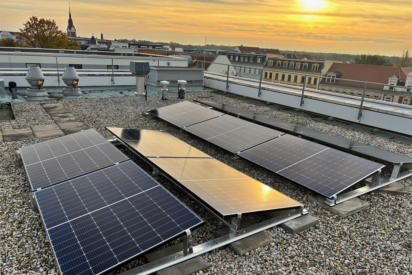 Foto von PV-Elementen für das Wärmepumpenmonitoring auf einem Dach im Hintergrund wolkenverhangener Sonnenuntergang über Leipzig
